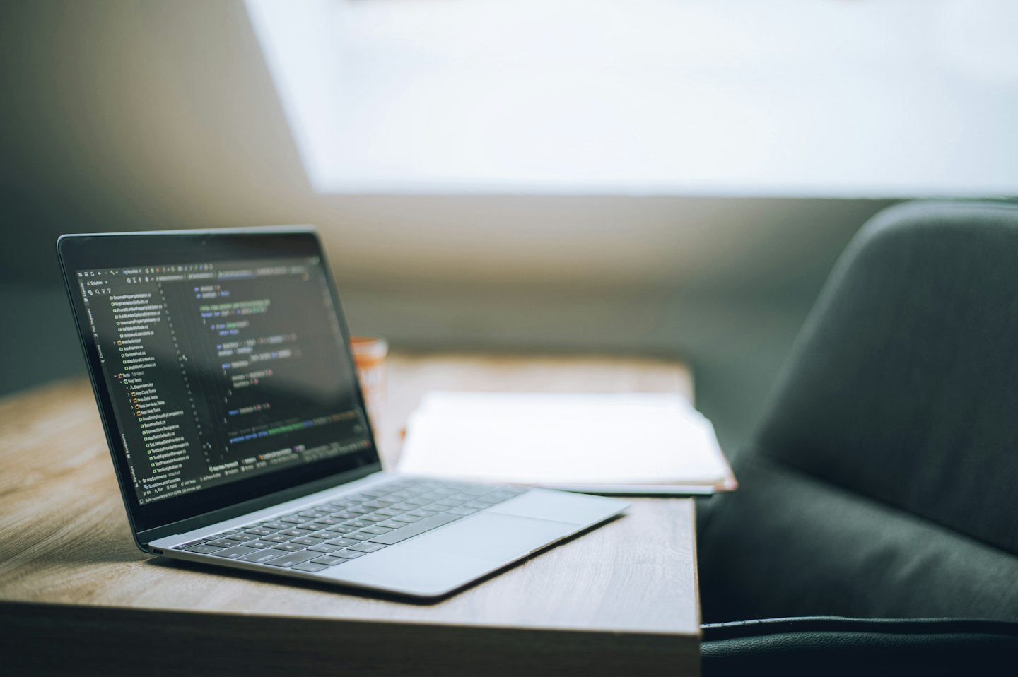 Laptop displaying programming code sits on a wooden desk.